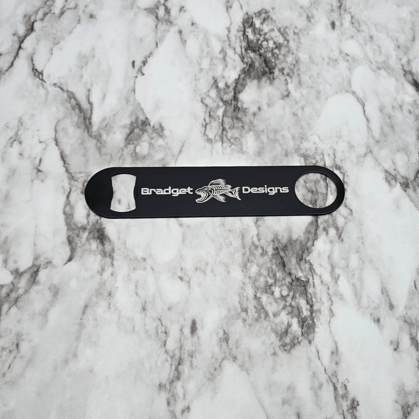 Black bottle opener with 'Bradget Designs' logo on a marble surface
