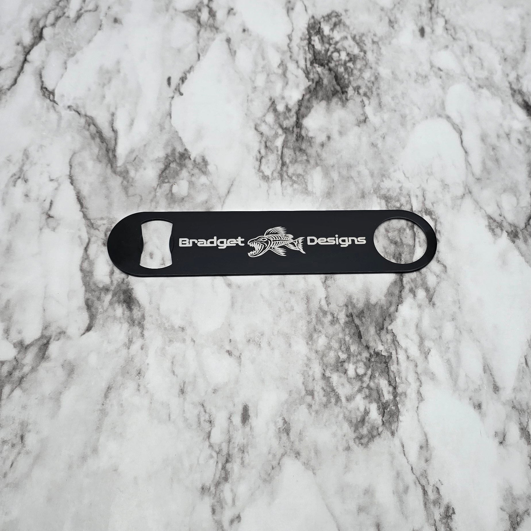 Black bottle opener with 'Bradget Designs' logo on a marble surface