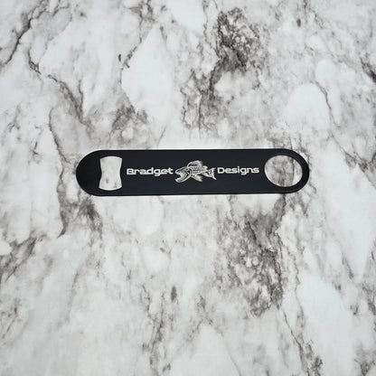 Black bottle opener with 'Bradget Designs' logo on a marble surface