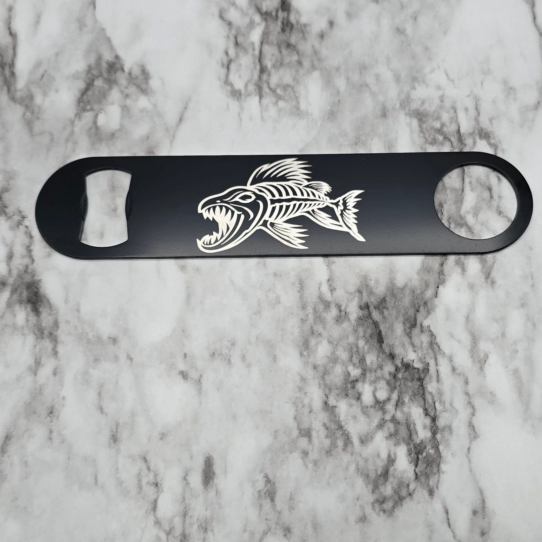 Black bottle opener with a fish design on a marble surface